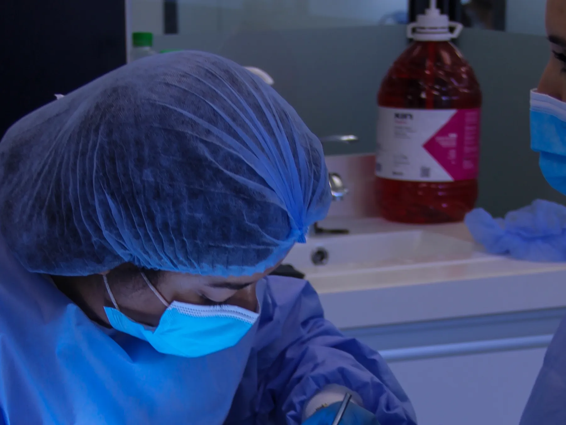 Opératrice en casaque et charlotte, sous le scialytique, pendant un acte de chirurgie orale